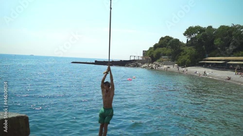 A young guy on a bungee swinging and jumping into the sea doing somersaults.