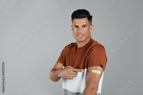 Vaccinated man showing medical plaster on his arm against grey background