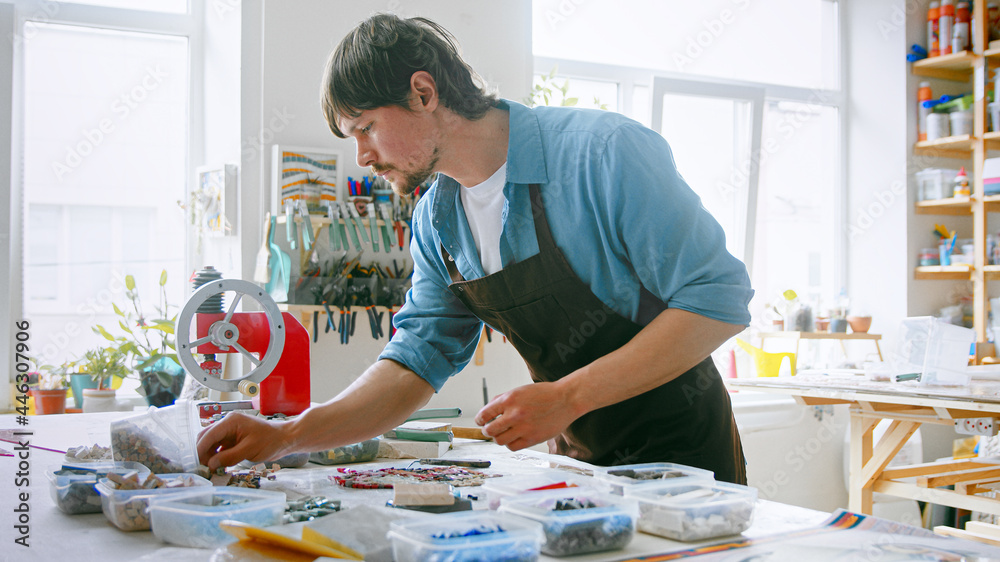 Young man with mosaic in workshop. Young master in an apron at work Young man with mosaic in workshop. Young master in an apron at work