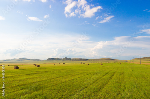 Summer landscape with hay bales on farming fields against the background of awesome cloudy sky and green hills in Khakassia, Russia