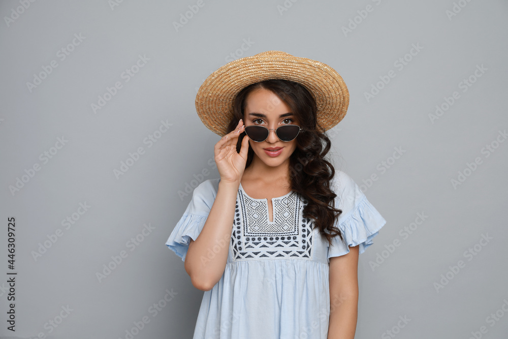 Beautiful young woman with straw hat and stylish sunglasses on light grey background