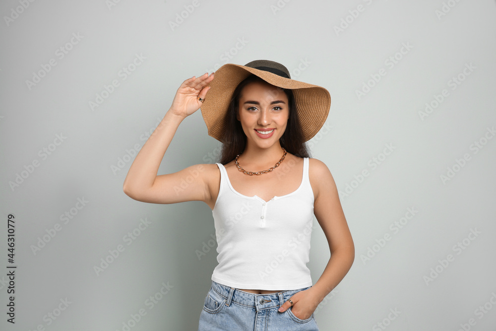Beautiful young woman wearing straw hat on light grey background. Stylish headdress Beautiful young woman wearing straw hat on light grey background. Stylish headdress