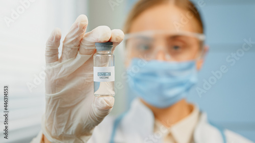 Blurred young woman medical nurse in disposable mask and glasses holds coronavirus vaccine
