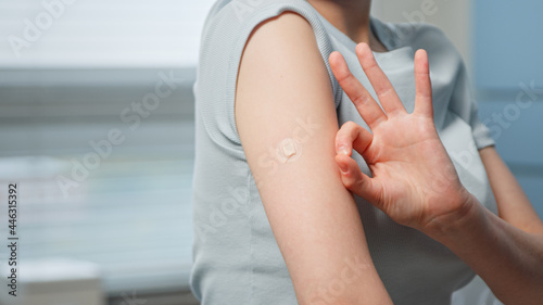 Young woman patient shows OK gesture with fingers near small injection spot on forearm skin