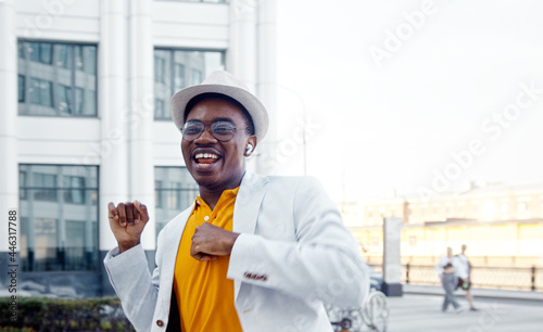 Inspired black actor in stylish suit dances and sings on city square with highrise buildings under sunlight © AboutLife