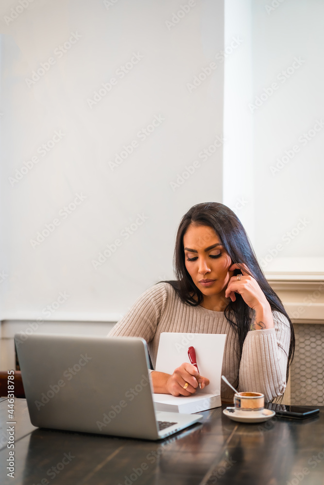 Brunette girl teleworking in a cafeteria with laptop, taking notes in online meeting, vertical photo Brunette girl teleworking in a cafeteria with laptop, taking notes in online meeting, vertical photo