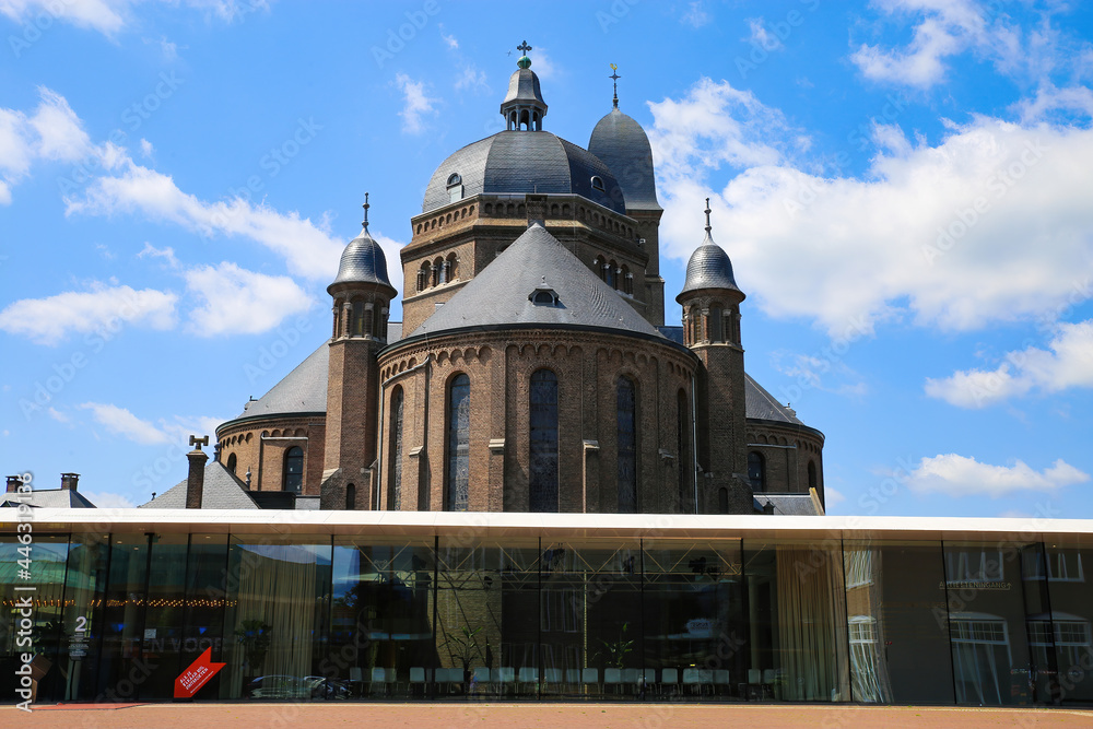 Helmond, Netherlands - July 10. 2021: View over square on transparent modern glass pavilion ( theater speelhuis) with old church against blue sky in summer