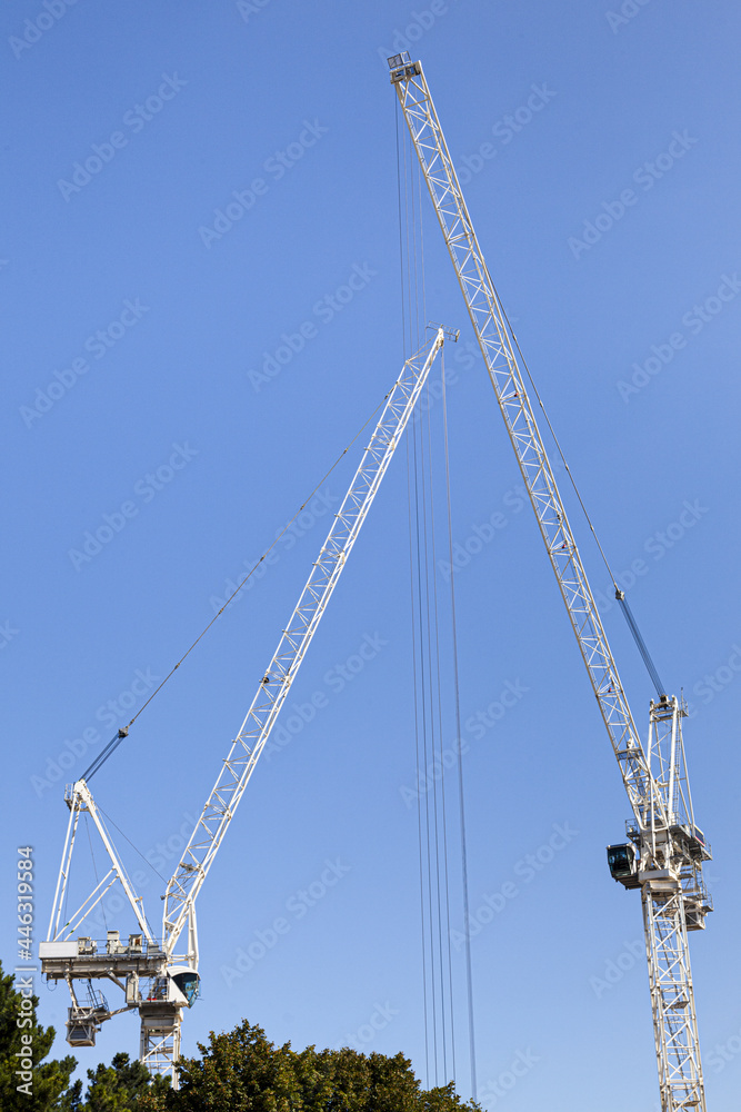 Two white construction cranes against a blue sky Two white construction cranes against a blue sky