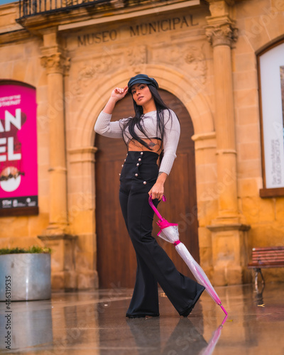 Posing of a young brunette Latina with a leather hat and black pants enjoying an autumn rainy day