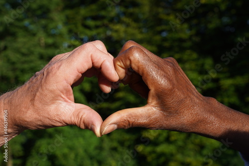 Multiracial hand heart in sunlight with green leaf background. Symbol for love, anti racism, acceptance and integration. photo