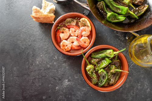 Spanish tapa bowls with fried pimientos or padron peppers and shrimps with lemon and herbs on a gray slate background, copy space, high angle view from above photo