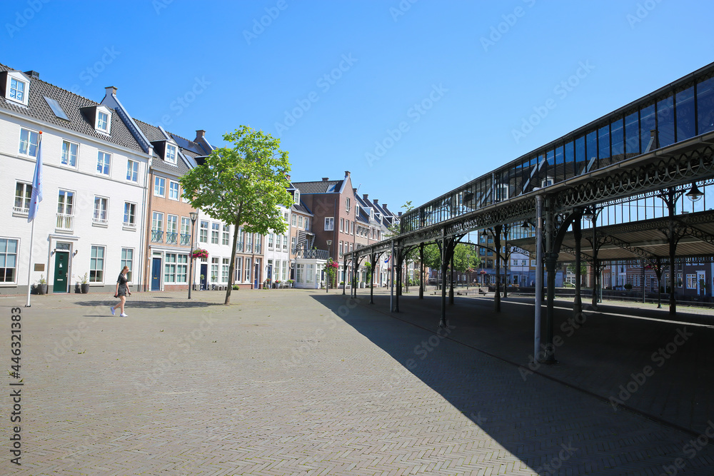 Helmond, Netherlands - July 10. 2021: View beyond open market hall construction on square with traditional dutch houses in summer with blue sky Helmond, Netherlands - July 10. 2021: View beyond open market hall construction on square with traditional dutch houses in summer with blue sky