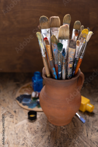 Paint brush in clay jug and palette on table background. Paintbrush for painting as art still life