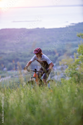 Obraz na płótnie Cyclist Riding Down a mountain at Sunrise with Beautiful lake in the Background. Extreme Sport and Enduro Biking Concept. w salonie