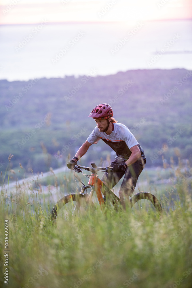 Cyclist Riding Down a mountain at Sunrise with Beautiful lake in the Background. Extreme Sport and Enduro Biking Concept.