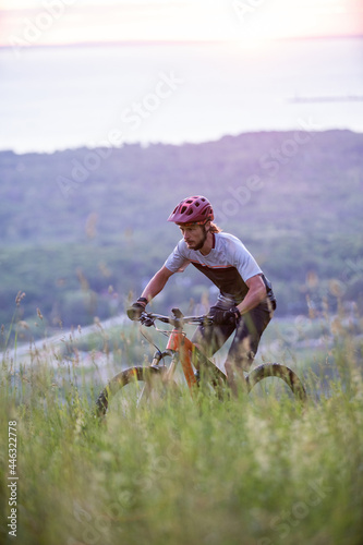 Obraz na płótnie Cyclist Riding Down a mountain at Sunrise with Beautiful lake in the Background. Extreme Sport and Enduro Biking Concept. w salonie
