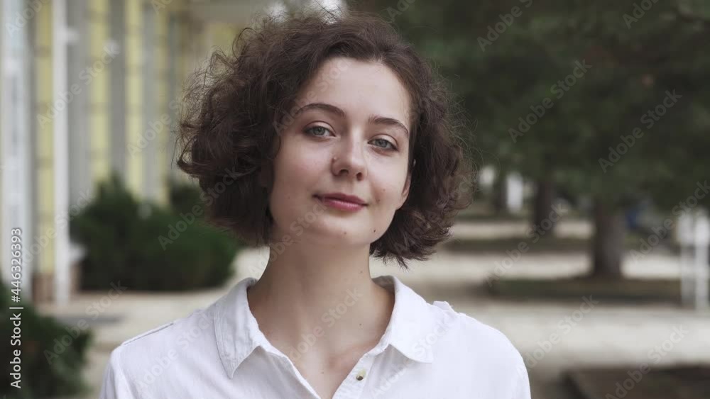 Beautiful curly brunette smiling on the street of the city. Charming appearance and smile. Positive emotion on the face of a young woman. Happy girl in a good mood stands on the street of the old city Beautiful curly brunette smiling on the street of the city. Charming appearance and smile. Positive emotion on the face of a young woman. Happy girl in a good mood stands on the street of the old city