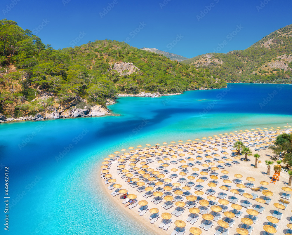 Aerial view of sea, sandy beach with umbrellas, forest, mountain at sunny day in summer. Blue lagoon in Oludeniz, Turkey. Tropical landscape with island, palms, white sandy bank, blue water. Top view
