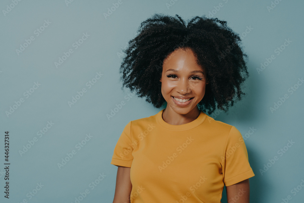 Happy dark skinned woman smiling at camera with pleased face expression, isolated on blue background Happy dark skinned woman smiling at camera with pleased face expression, isolated on blue background