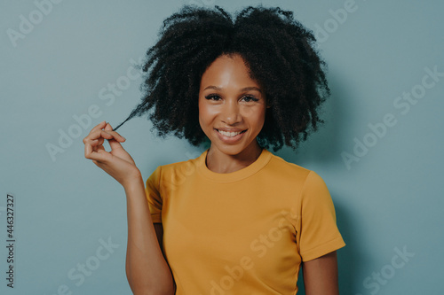 Studio portrait of beautiful young dark skinned woman with shaggy hairstyle smiling cheerfully