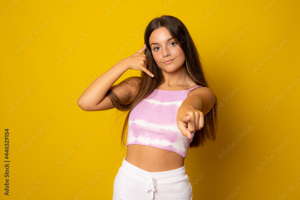 Young girl over yellow wall smiling doing phone gesture with hand and fingers like talking on the telephone. Communicating concepts. Young girl over yellow wall smiling doing phone gesture with hand and fingers like talking on the telephone. Communicating concepts.