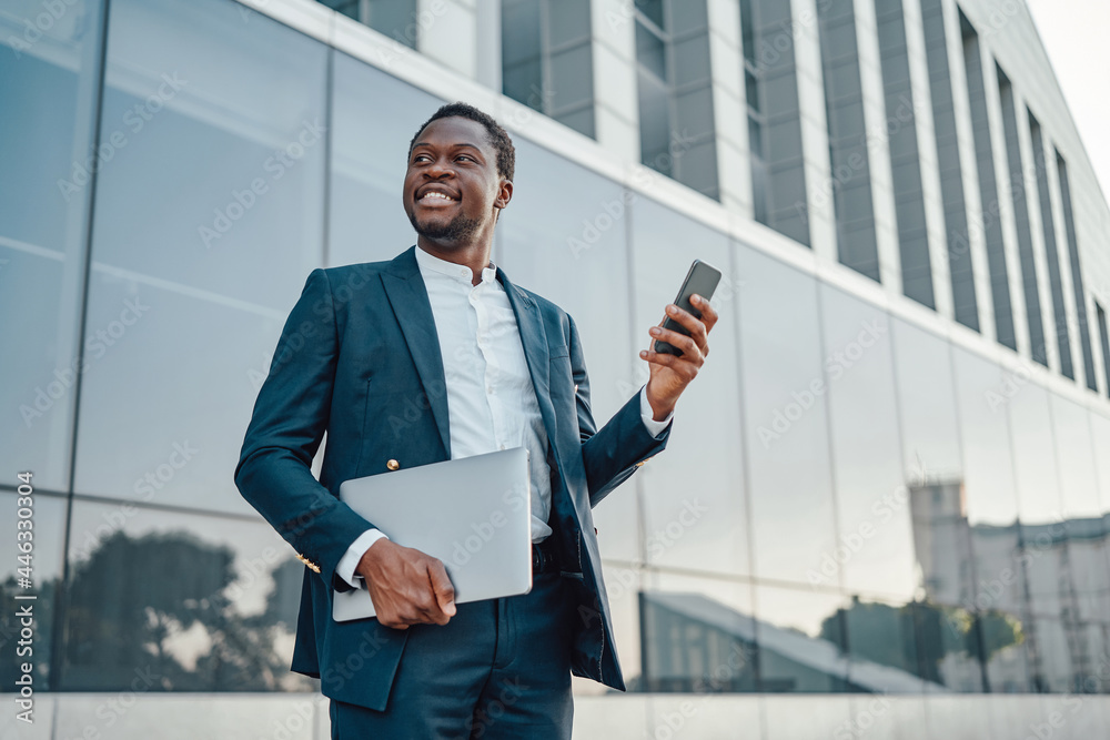 Fototapeta premium Joyful black businessman with laptop and smart phone