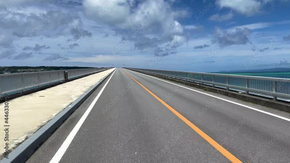OKINAWA, JAPAN - JUNE 2021 : Driving at Kouri Island bridge. Wide camera point of view (POV), seaside road driving shot. Blue sunny summer sky. OKINAWA, JAPAN - JUNE 2021 : Driving at Kouri Island bridge. Wide camera point of view (POV), seaside road driving shot. Blue sunny summer sky.
