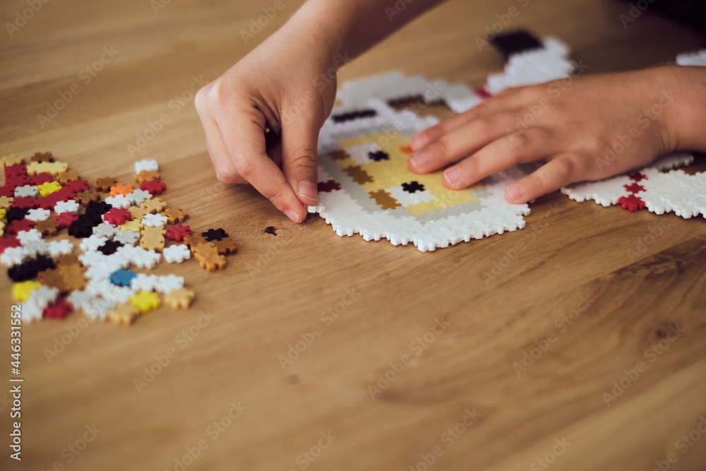 Child making the astronaut made of plastic puzzle tiles over the wooden table. Children's creative game at home Child making the astronaut made of plastic puzzle tiles over the wooden table. Children's creative game at home