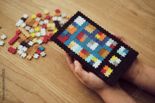 Child holding the tablet made of plastic puzzle tiles over the wooden table. Children's creative game at home