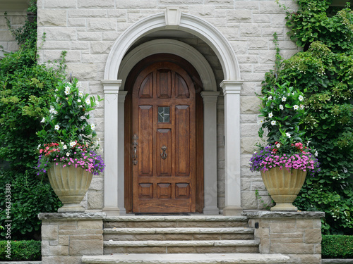 Elegant wood grain front door of stone house in round vestibule, surrounded by vines and flowers