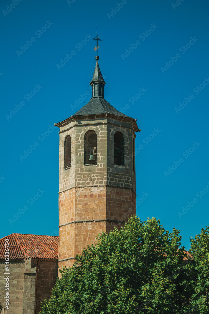 Church bell tower made of bricks and green trees with blue sky, in a sunny day at Avila. A cute city with medieval buildings in Spain.