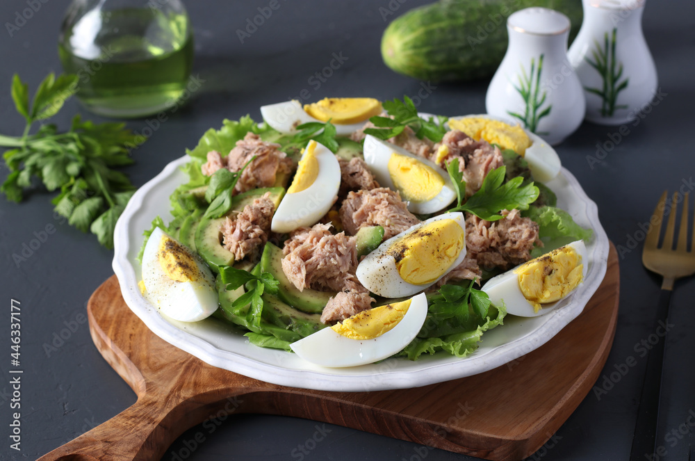 Healthy salad with avocado, tuna, eggs and cucumbers on a white plate on a wooden board