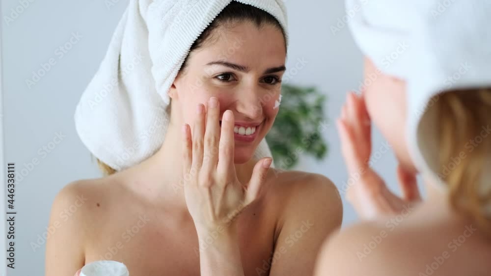 Video of beautiful young woman caring of her skin while putting on cream looking at mirror at home. Video of beautiful young woman caring of her skin while putting on cream looking at mirror at home.
