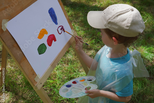 Obraz na plátně boy 3-4 years old draws on an easel with paints outdoors