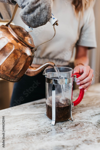 Woman pours hot water from teapot into a French press to make coffee