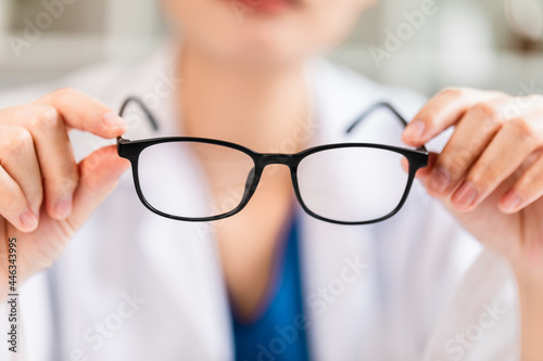 Close-up view of a female doctor holding and showing glasses lens, optics shop.