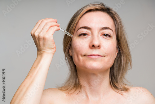 Happy mature woman putting oil under her eyes