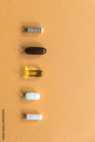 Different types of capsules and tablets with vitamins and dietary supplements on an orange background