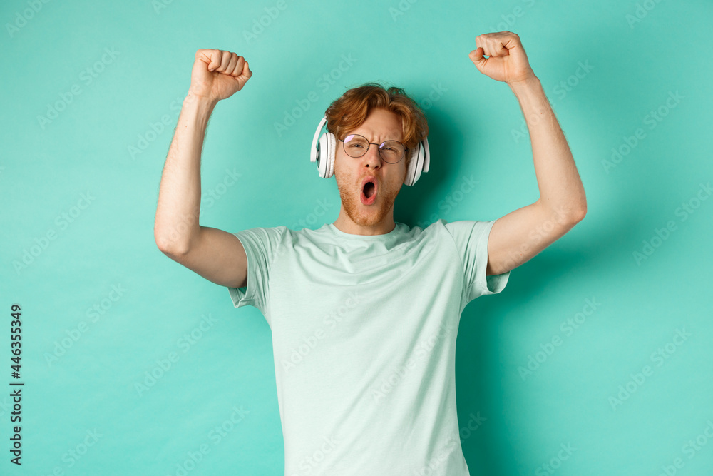 Lifestyle concept. Carefree guy with red hair, dancing and having fun,  listening music in headphones, standing over turquoise background Stock  Photo | Adobe Stock