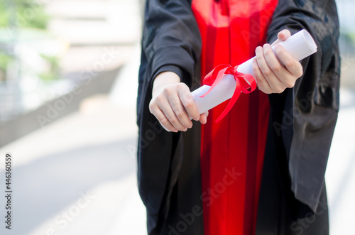 College or university student wearing black and red gown showing the deploma certificate, for educational success concept