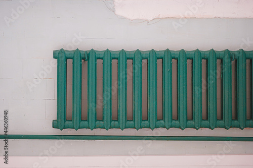 Old-fashioned green heating radiator on a grey tile wall. Indoor heating system. 