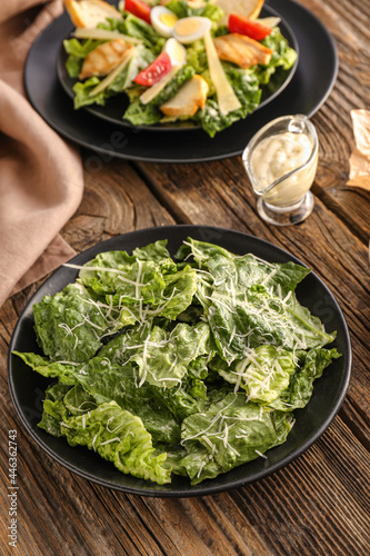Plates with tasty Caesar salad and sauce on wooden background