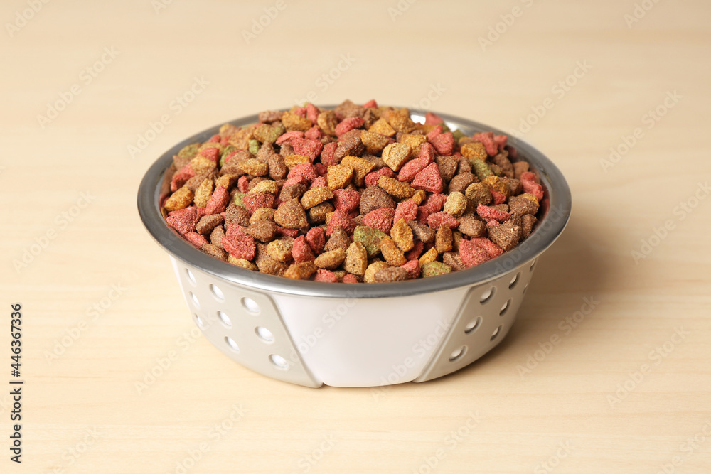 Dry dog food in pet bowl on wooden surface