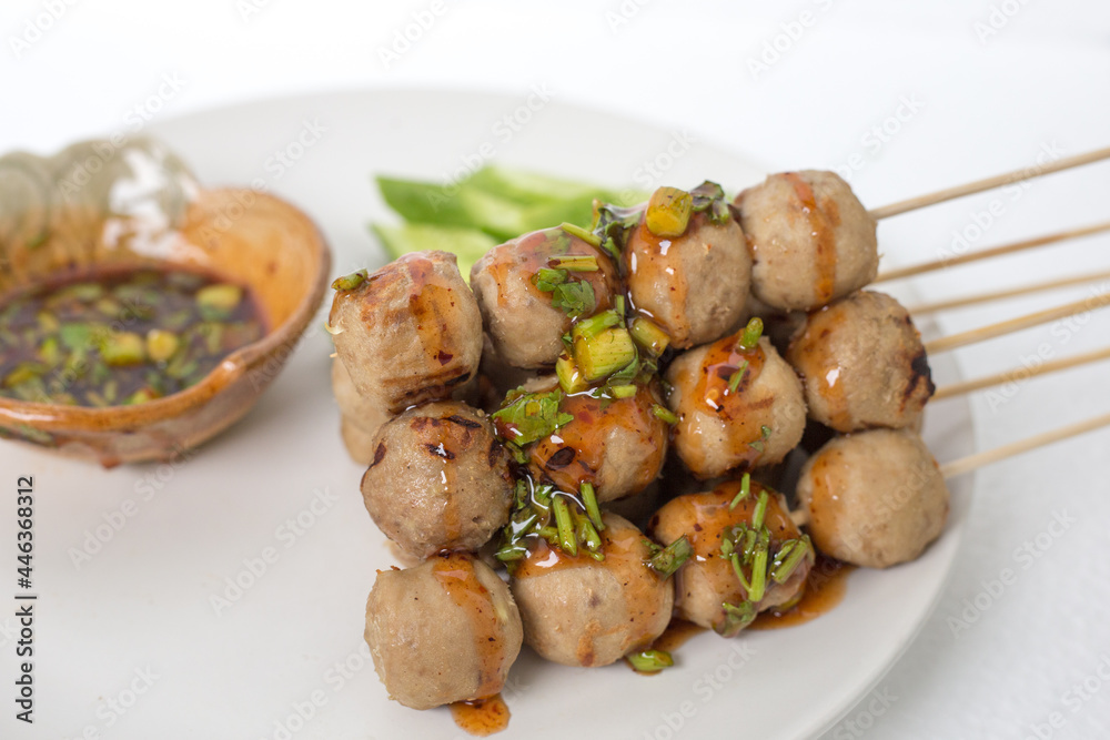 Grilled meatballs, skewers, meatballs, noodles with vegetables and dipping sauces burnt on plate and white Asian food.
