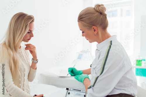 Young woman beautician talking with a young blond woman about new facial skin care procedures  Professional cosmetician examining face skin