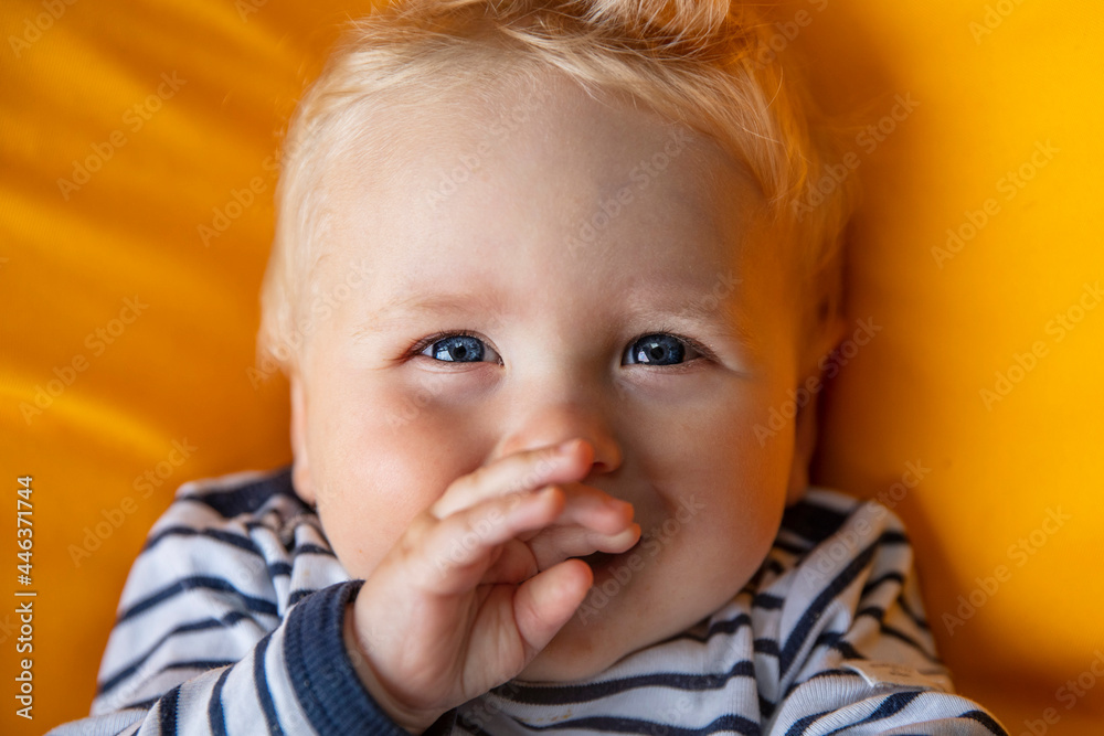Close up of a cute 9 month old baby boy with blue eyes on a yellow background Close up of a cute 9 month old baby boy with blue eyes on a yellow background