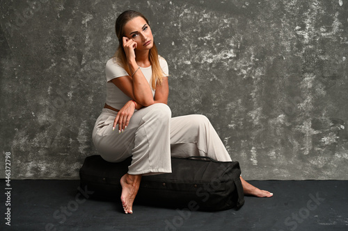 Horizontal high resolution photo of a skinny caucasian girl model sitting in a studio on a gray background