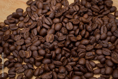 Many coffee beans placed around  in a warm on wood background.