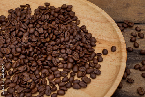 Many coffee beans placed around on a wooden dish in a warm on wood background.