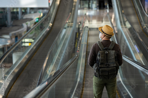 Traveler man wearing mask protect flu coronavirus. Tourist in airport terminal standing at escalator. During the pandemic must be social distancing self quarantine.